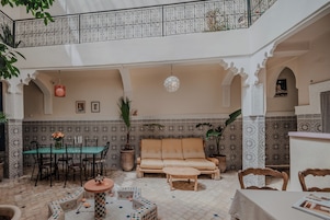 Un interior amplio con techo alto, comedor, zona de estar con sofá y reposapiés, y techo decorativo con lámpara colgante.
