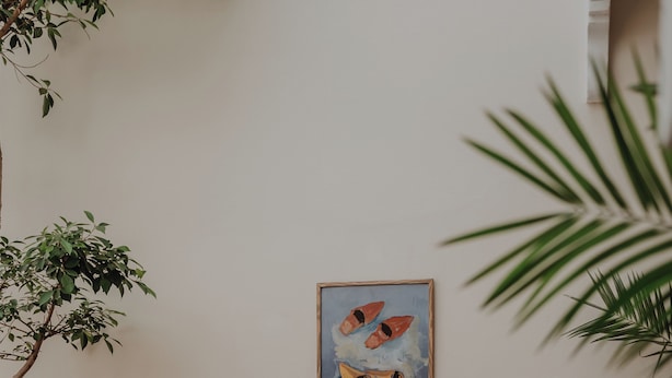 A small patio area with two wooden chairs, a round table, a vase with flowers, and a painting on the wall. - Riad Imndi (Marrakech)