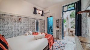 A hotel room with a patterned tile wall, a bed with a red and black blanket, a wooden nightstand, and a view of a courtyard through an open door. - Riad Imndi (Marrakech)