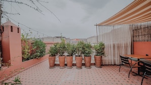 A rooftop terrace with potted plants, a table, and chairs. - Riad Imndi (Marrakech)