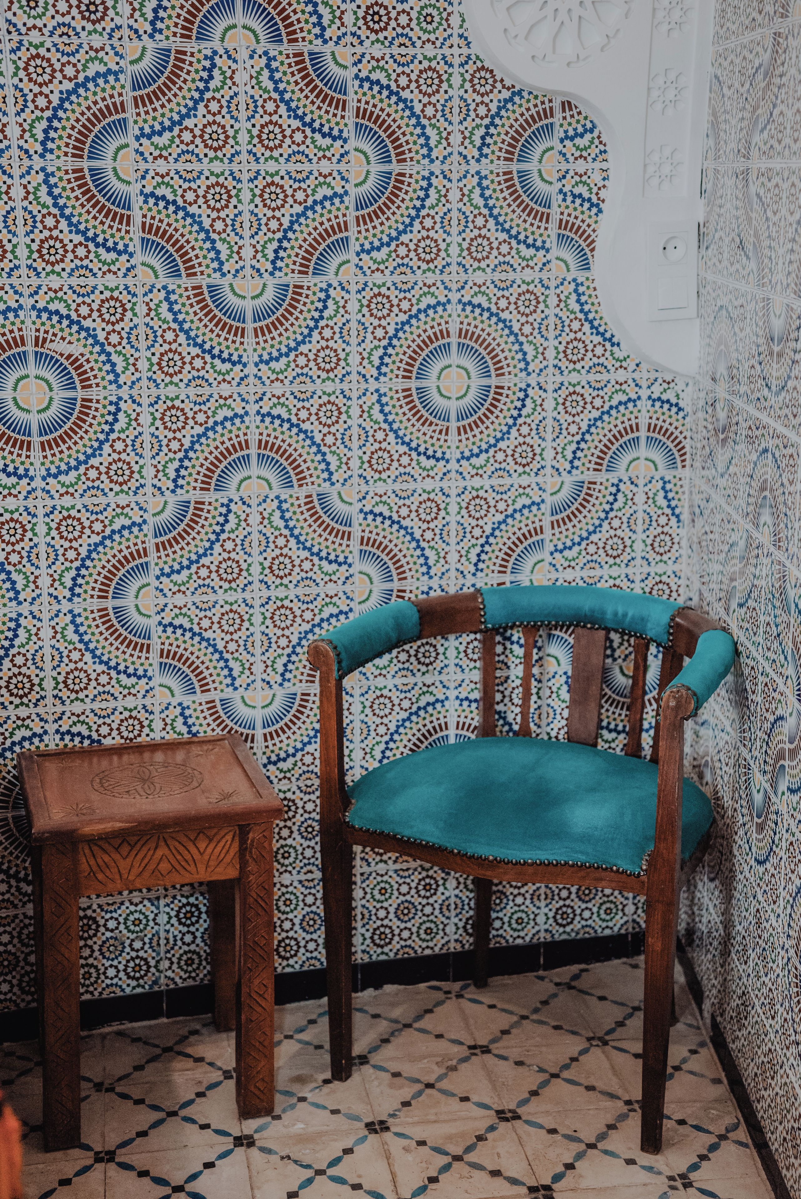 A room with a patterned tile wall, a wooden chair with a cushion, and a small wooden table.