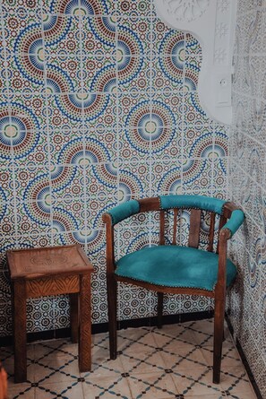 A room with a patterned tile wall, a wooden chair with a cushion, and a small wooden table.