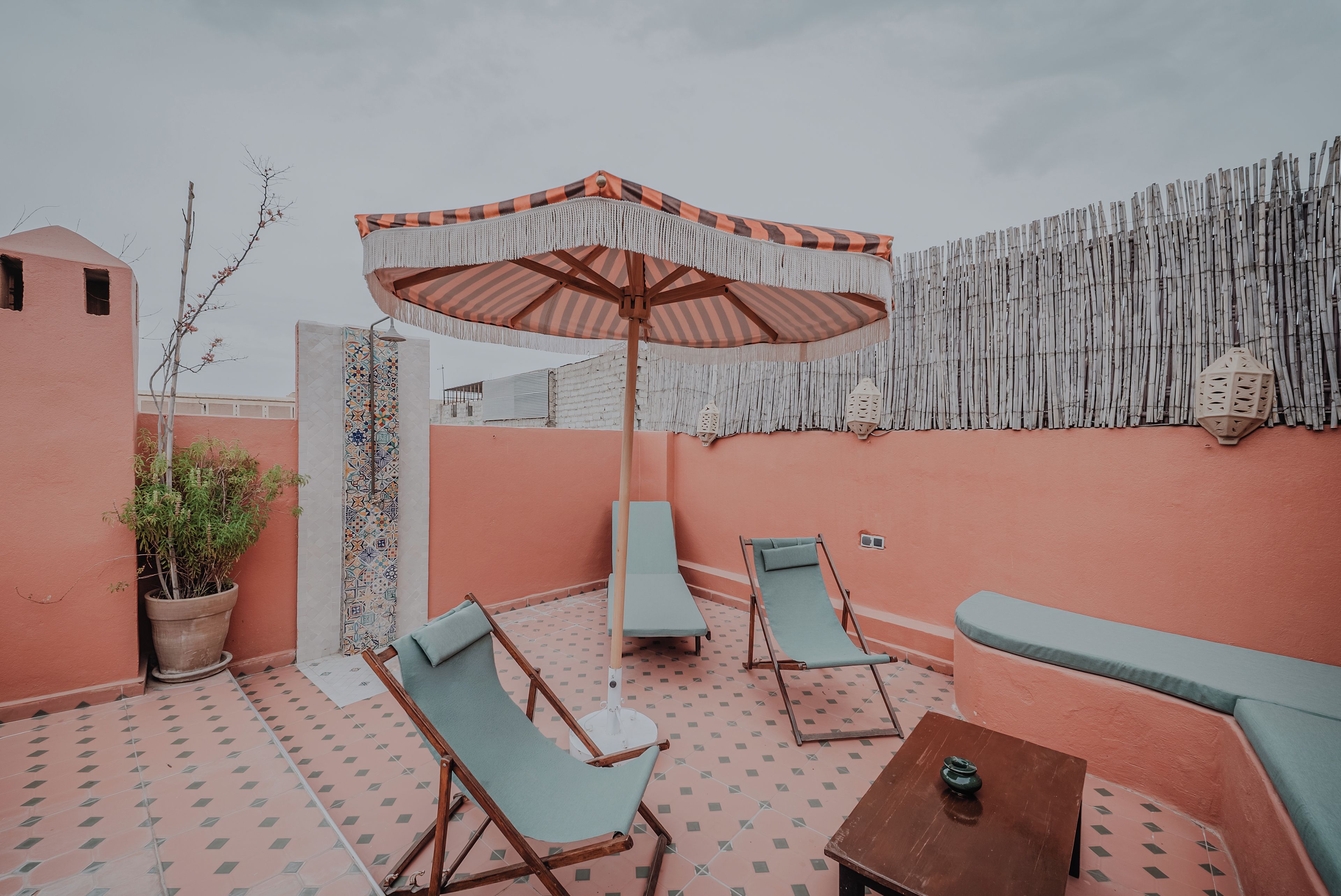 An outdoor seating area with a patterned floor, a striped umbrella, and a wall with vertical bamboo slats.