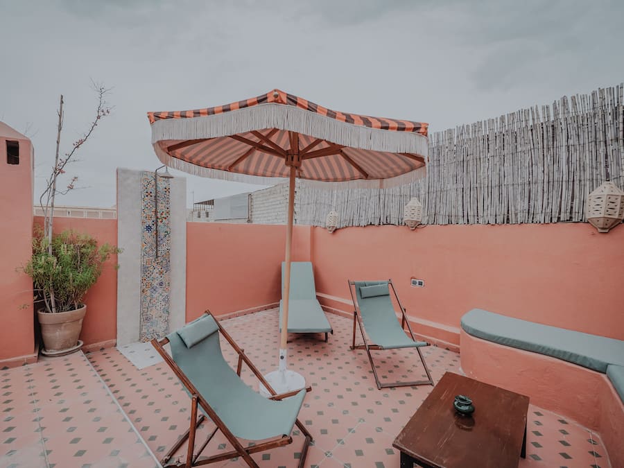 Un área de estar al aire libre con piso estampado, un paraguas a rayas y una pared con listones verticales de bambú.