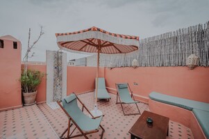 Un área de estar al aire libre con piso estampado, un paraguas a rayas y una pared con listones verticales de bambú.