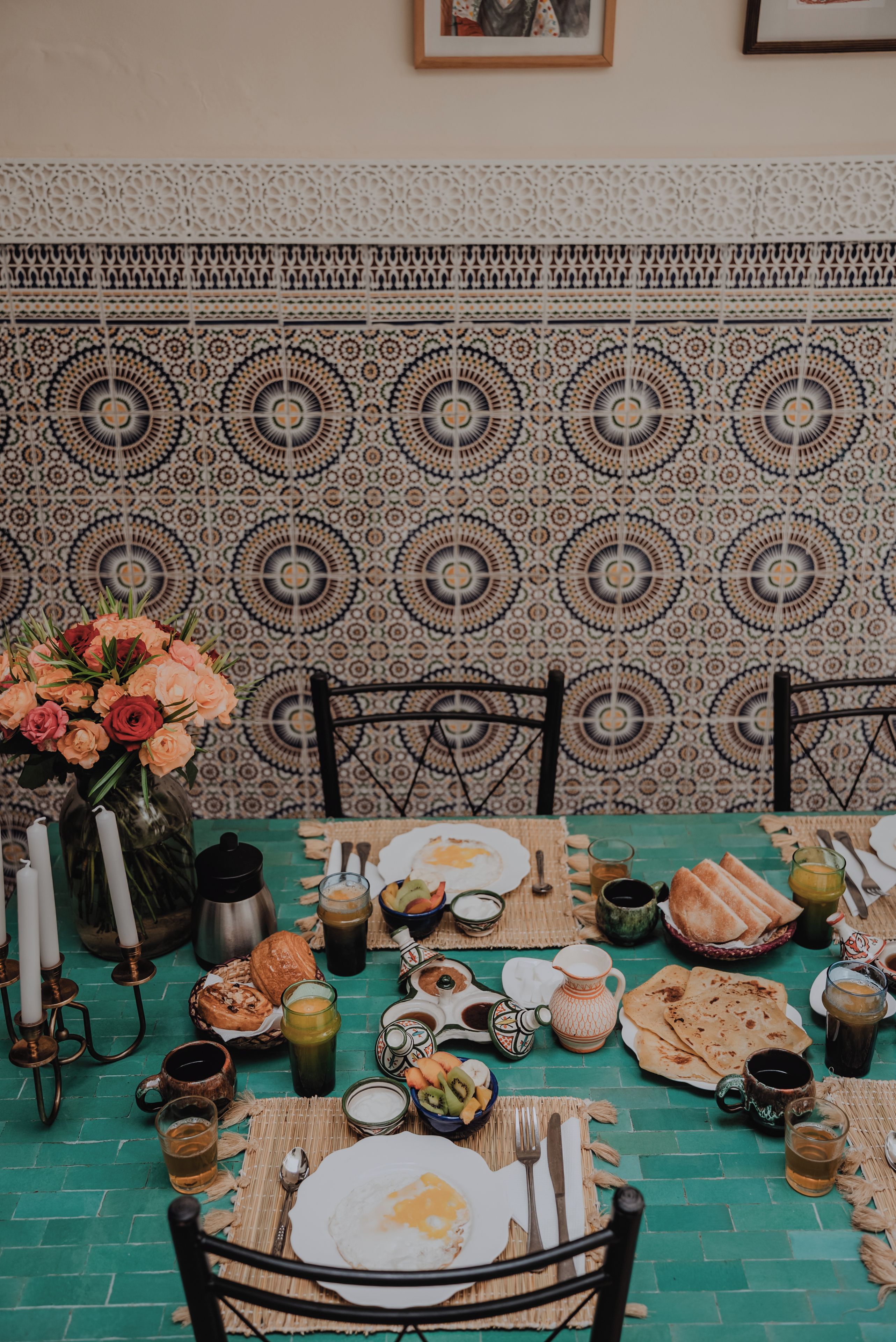 Una mesa de comedor dispuesta con diversos platos, un jarrón de flores y una pared con diseño en el fondo.