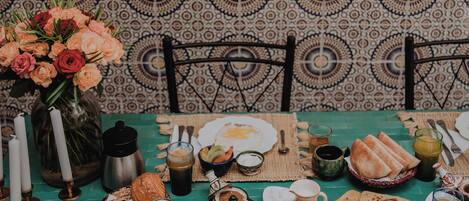 Una mesa de comedor dispuesta con diversos platos, un jarrón de flores y una pared con diseño en el fondo.