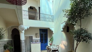Un amplio patio con zona de comedor, un gran árbol en maceta y un balcón con barandillas decorativas.