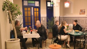 Un comedor con mesas y sillas, una planta en maceta y piso de baldosas.