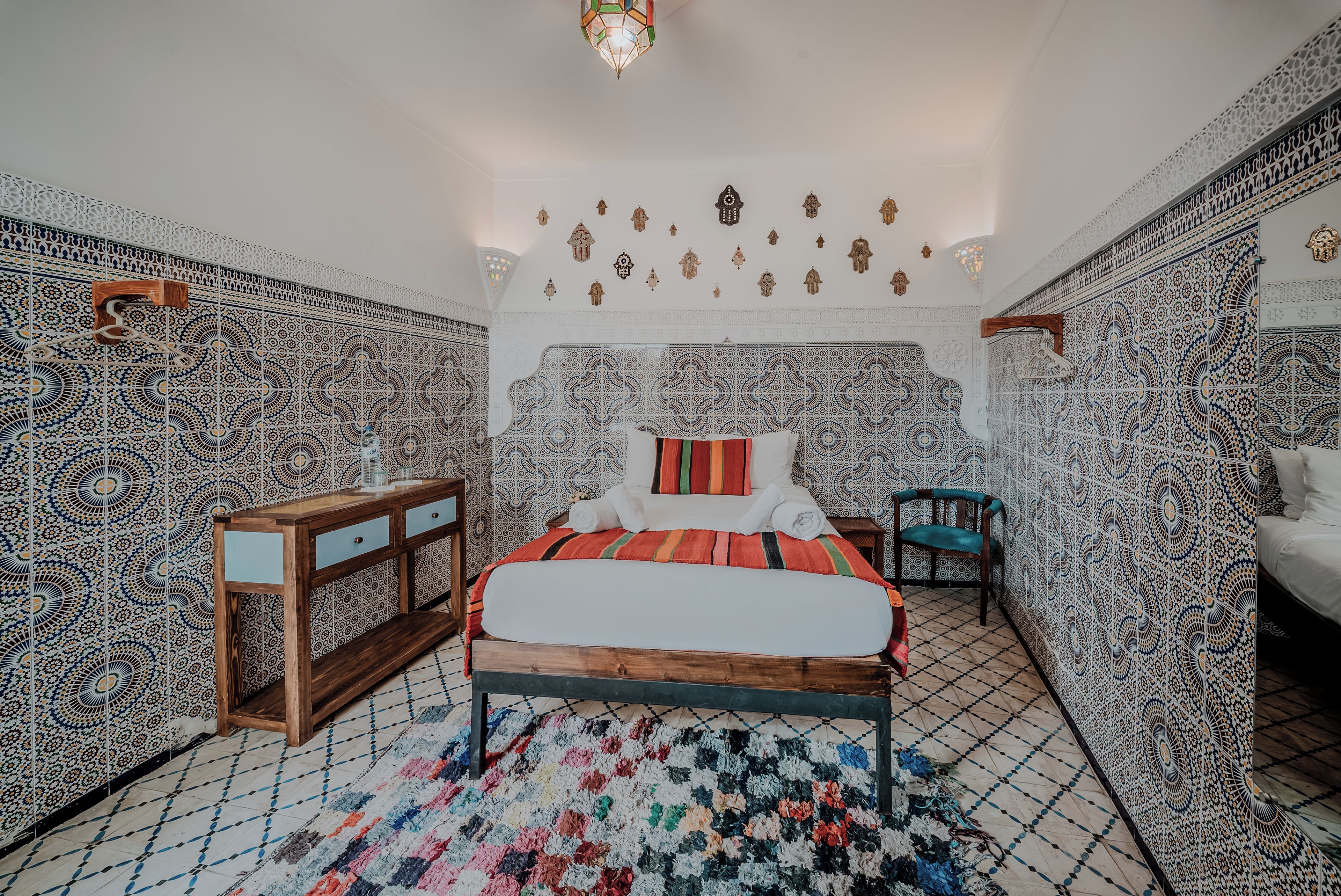 A room with a patterned floor, a bed with a red and white bedspread, a wooden nightstand, and a chair.