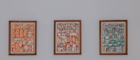 A white wall with three framed artworks and a white sofa with an orange patterned pillow.