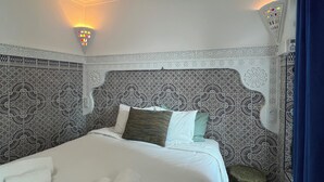 Habitación de hotel con una cama grande, paredes estampadas y una mesita auxiliar.