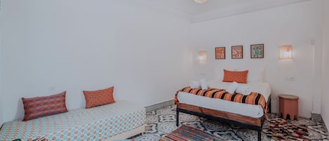 Une chambre avec deux lits, une literie à motifs, un tapis coloré et des lampes fixées au mur.