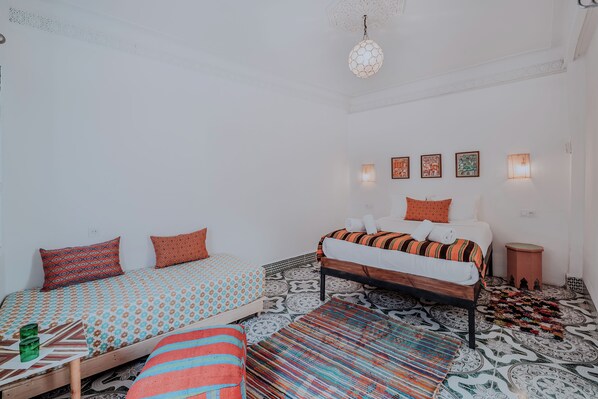A room with two beds, patterned bedding, a colorful rug, and wall-mounted lights.