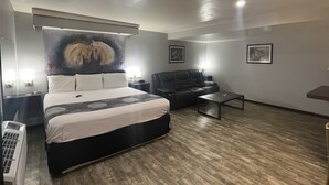 A modern hotel room with a large bed, a leather sofa, a small table, and a wall-mounted TV. - Cindy Lyn Motel (Cicero)