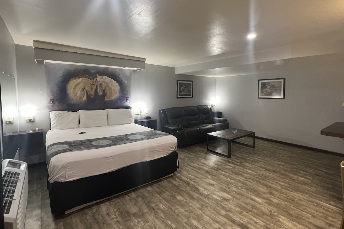A modern hotel room with a large bed, a leather sofa, a small table, and a wall-mounted TV.