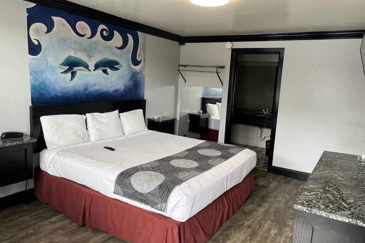 A hotel room with a bed, a nightstand, a painting of whales, a bathroom mirror, and a marble countertop.