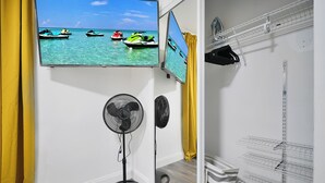 A room with a large window displaying a beach scene, a standing fan, and a white shelving unit. - Good Vibes Retreat Decor BBQ Patio heart Wynwood (Miami)