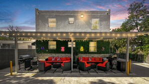 A covered outdoor patio with a barbecue grill, red cushioned seating, and string lights. - Good Vibes Retreat Decor BBQ Patio heart Wynwood (Miami)