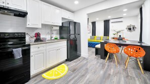 A modern kitchen with white cabinets, a black refrigerator, and a dining area with orange chairs. - Good Vibes Retreat Decor BBQ Patio heart Wynwood (Miami)