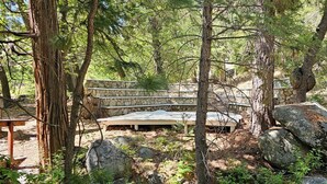 Ein rustikaler Sitzbereich im Freien mit Steinsitzen und einer Steinmauer, umgeben von Bäumen und Steinen.
