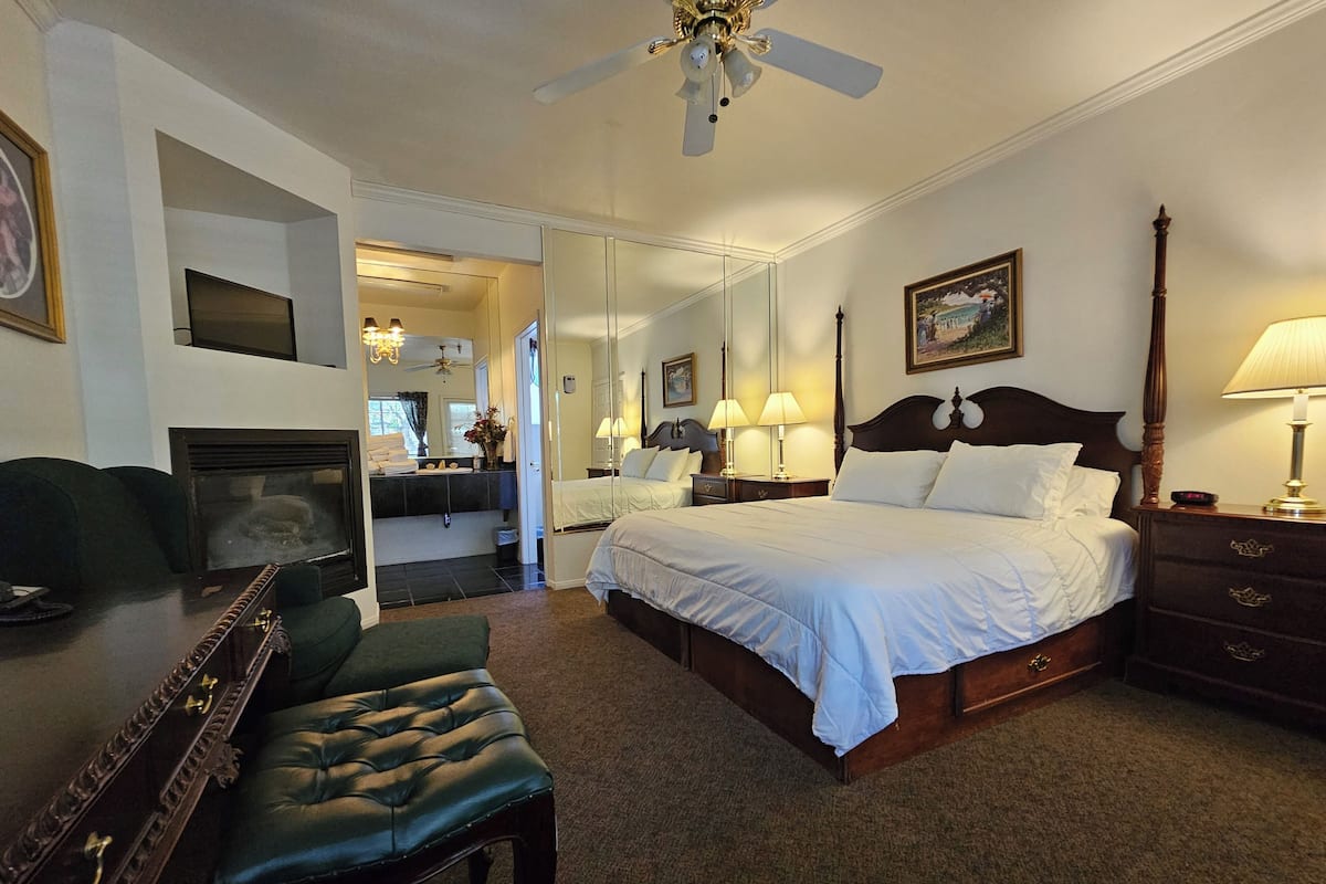 A hotel room with a large bed, a desk with a chair, a mirror, a dresser, and a ceiling fan.