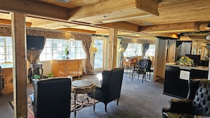 Ein gemütlicher Raum mit Holzbalkendecke, einer Rezeption, einem schwarzen Ledersofa und einem kleinen runden Tisch.