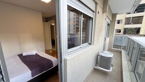 A modern bedroom with a bed, a window, and a balcony with a trash bin. - Lockings  Lourdes 12 (Belo Horizonte)