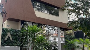 A modern building with a geometric facade, large windows, and a small courtyard with palm trees and a water feature. - Lockings  Lourdes 12 (Belo Horizonte)