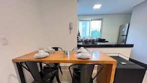A compact kitchen with a dining table set for two, black chairs, and a small refrigerator. - Lockings  Lourdes 12 (Belo Horizonte)
