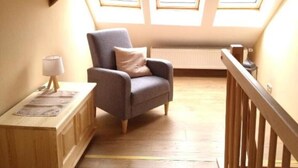 A cozy attic room with a wooden floor, a grey armchair, a small table with a lamp, and a view through skylights. - Narrow & tall - Welcome to the narrowest house in Bad Frankenhausen (Bad Frankenhausen/Kyffhäuser)