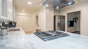 Et moderne køkken med en central ø, rustfrie hvidelementer og stålhvide skabe.