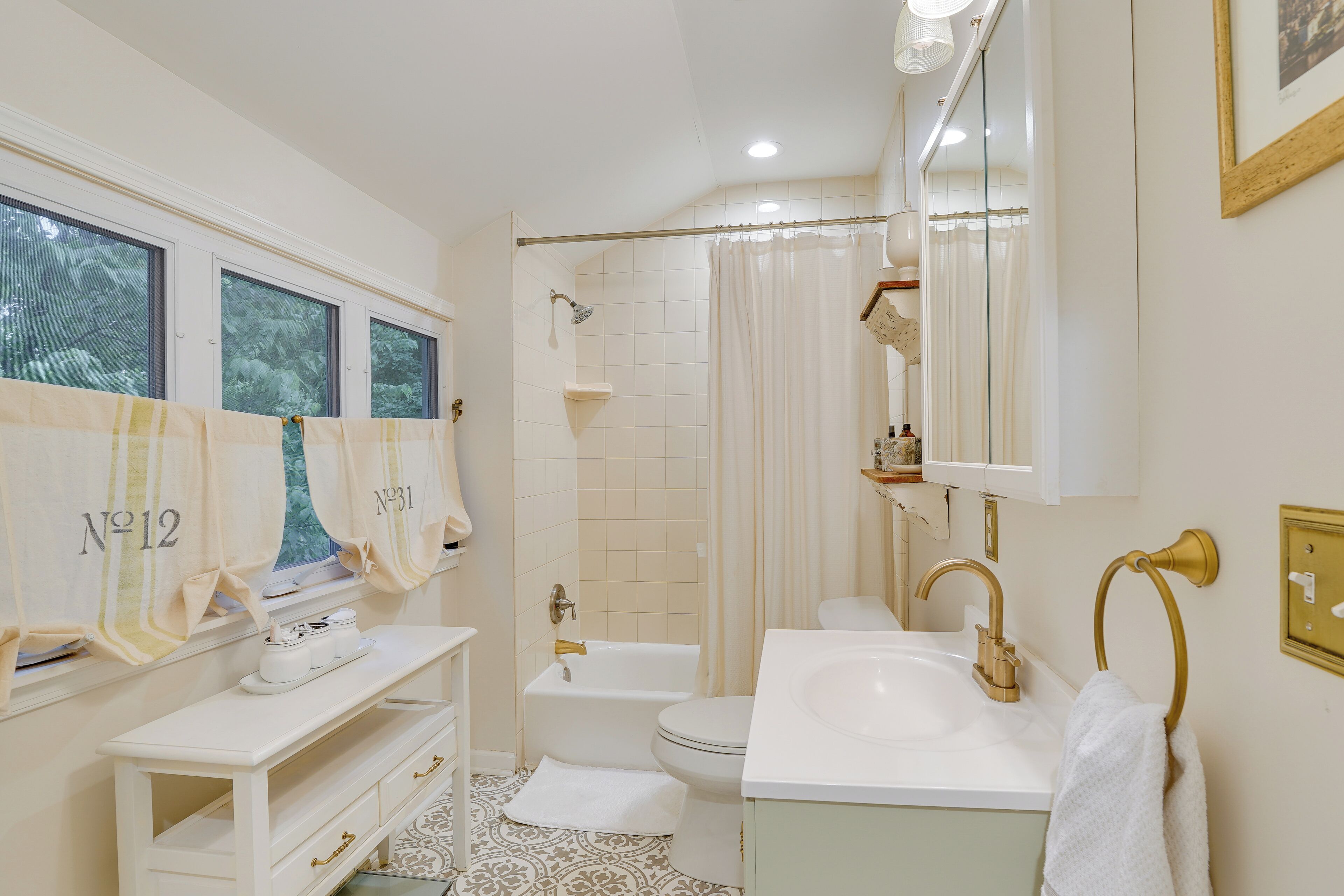 A bathroom with a bathtub, toilet, and sink. There are towels hanging on the wall and a vanity with drawers.