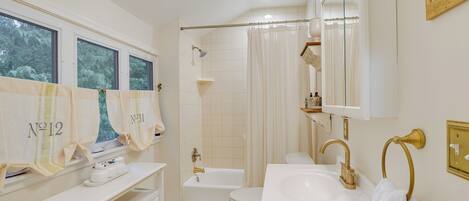 A bathroom with a bathtub, toilet, and sink. There are towels hanging on the wall and a vanity with drawers.