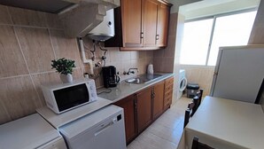 A compact kitchen with a microwave, oven, sink, and a small countertop. - Lisbon traditional T2 with balcony in Damaia (Amadora)
