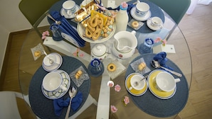 Ein runder Glastisch ist für eine Mahlzeit gedeckt, mit blauen Tischsets, blau-weißem Geschirr und verschiedenen Speisen und Getränken.