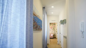 Ein Flur mit einem blauen Vorhang, einem Stadtbildgemälde, einer floralen Wanddekoration und einem Telefon an der Wand.