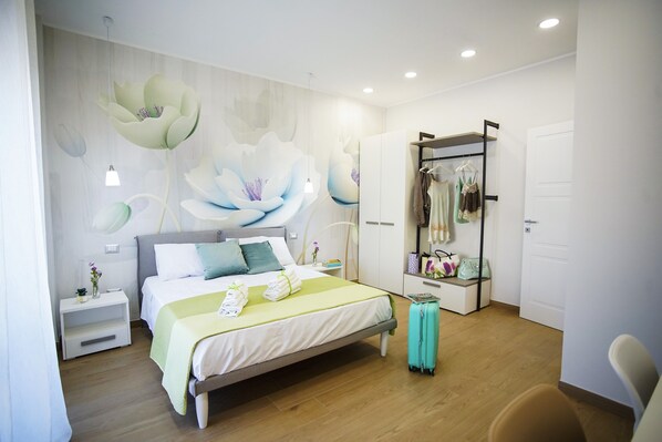 A modern hotel room with a large bed, a wardrobe, a seating area, and a wall with a floral mural. - 3-Bedroom Apartment in Castellammare di Stabia (Castellammare di stabia)