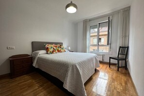 A bedroom with a bed, a nightstand, a chair, a window with curtains, and a radiator. - 632A Beautiful Apartment in Oviedo by R2R (Oviedo)
