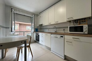 A kitchen with white cabinets, a microwave, a dishwasher, and a dining table with chairs. - 632A Beautiful Apartment in Oviedo by R2R (Oviedo)