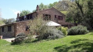 Ein rustikales Steinhaus mit geneigtem Dach, umgeben von viel Grün und Bäumen.