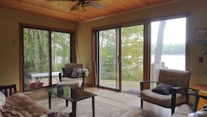 Un vaste salon doté d’un ventilateur de plafond, de grandes portes-fenêtres coulissantes donnant sur une terrasse et offrant une vue sur un lac.
