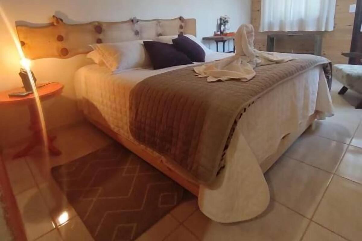 A bedroom with a wooden ceiling, a bed with a beige bedspread, a nightstand, and a window with curtains.