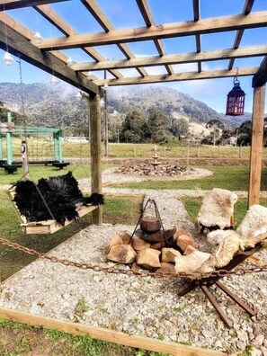 A wooden pergola with a rustic fire pit and seating area, surrounded by a gravel path and a fenced enclosure. - Pousada Nó de Pinho Urubici (Urubici)