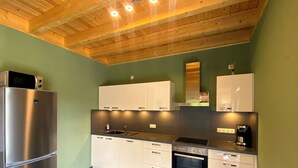 Een moderne keuken met een roestvrijstalen koelkast, witte kastjes, een inbouwoven en een houten plafond.