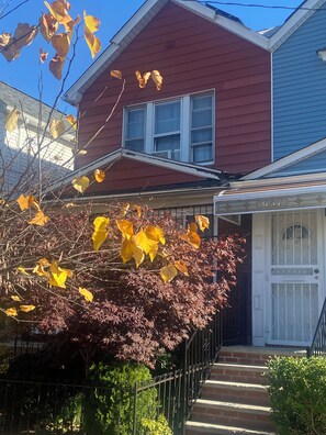 A two-story house with a red and blue exterior, a white front door, and a small front yard with a tree and a fence.