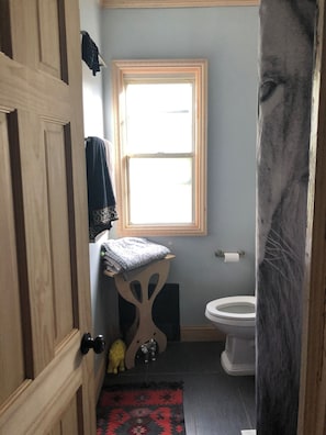 A bathroom with a toilet, a window, a towel rack, and a small shelf with a towel.