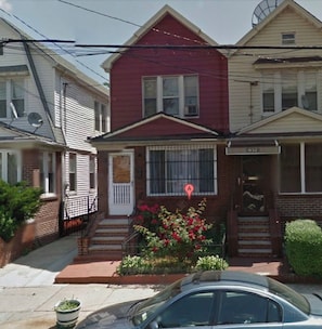 A two-story house with a red front door, a small front yard with flowers, and a mailbox.