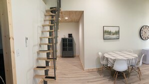 Una escalera con acabados de madera, un comedor con mesa y sillas, un armario gris, un reloj y un cuadro en la pared.