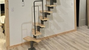 Una escalera de madera con barandillas de metal en una habitación con paredes de tonos claros y suelo de madera.